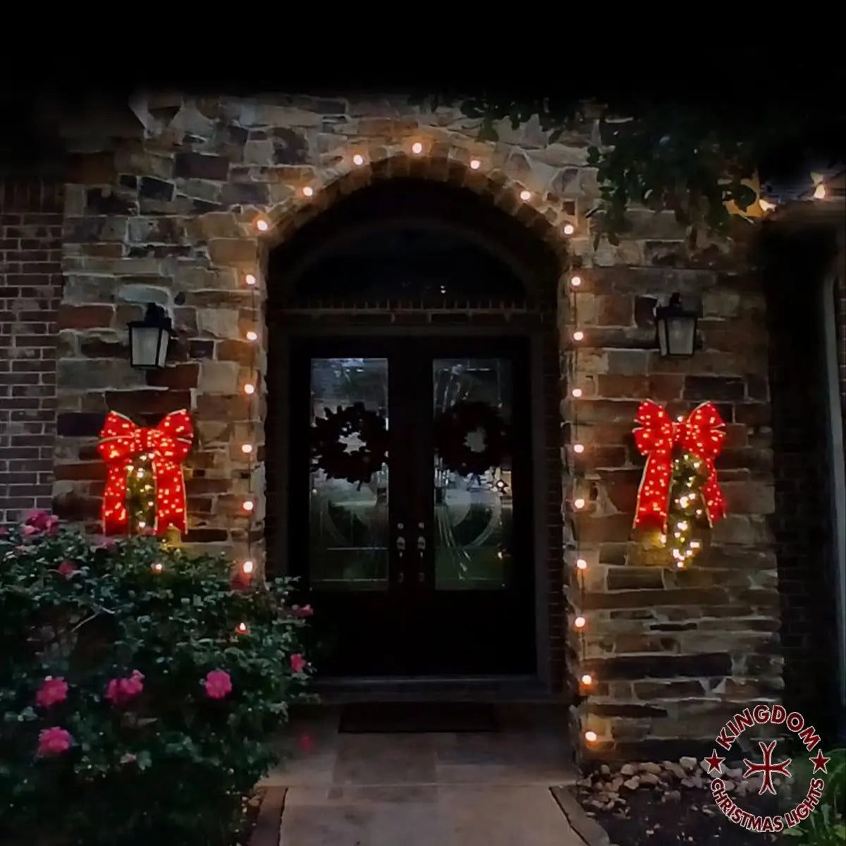 Residential front entry decorated with warm white Christmas lights, featuring an outlined arch and two illuminated holiday sprays with red bows.
