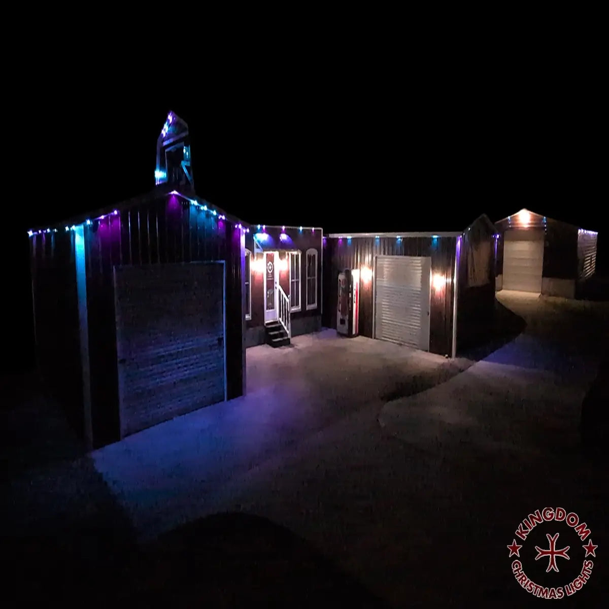 Building and detached garage with blue and purple permanent lighting beneath the eaves at night