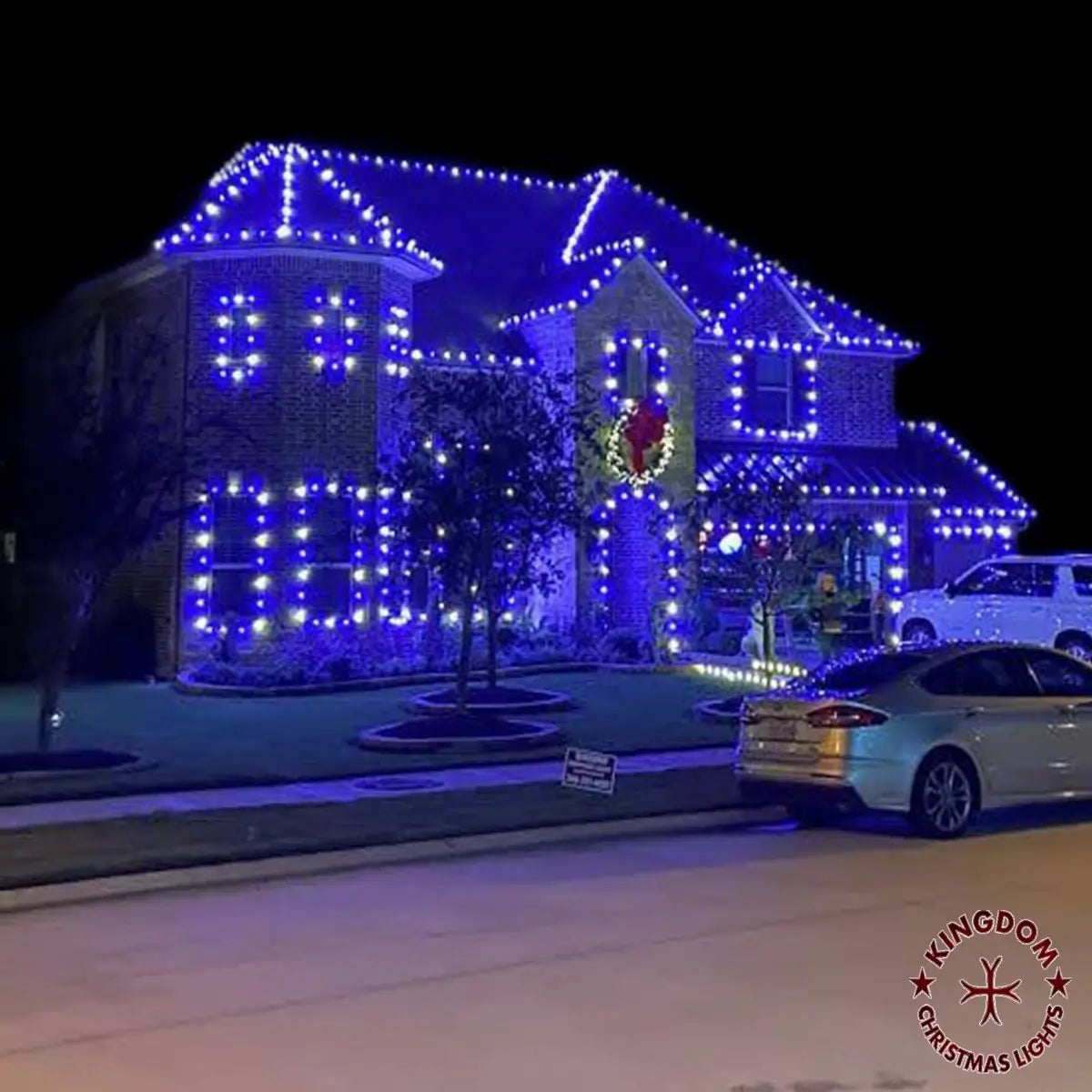 House decorated with Christmas lights at night, featuring a wreath and blue lights.