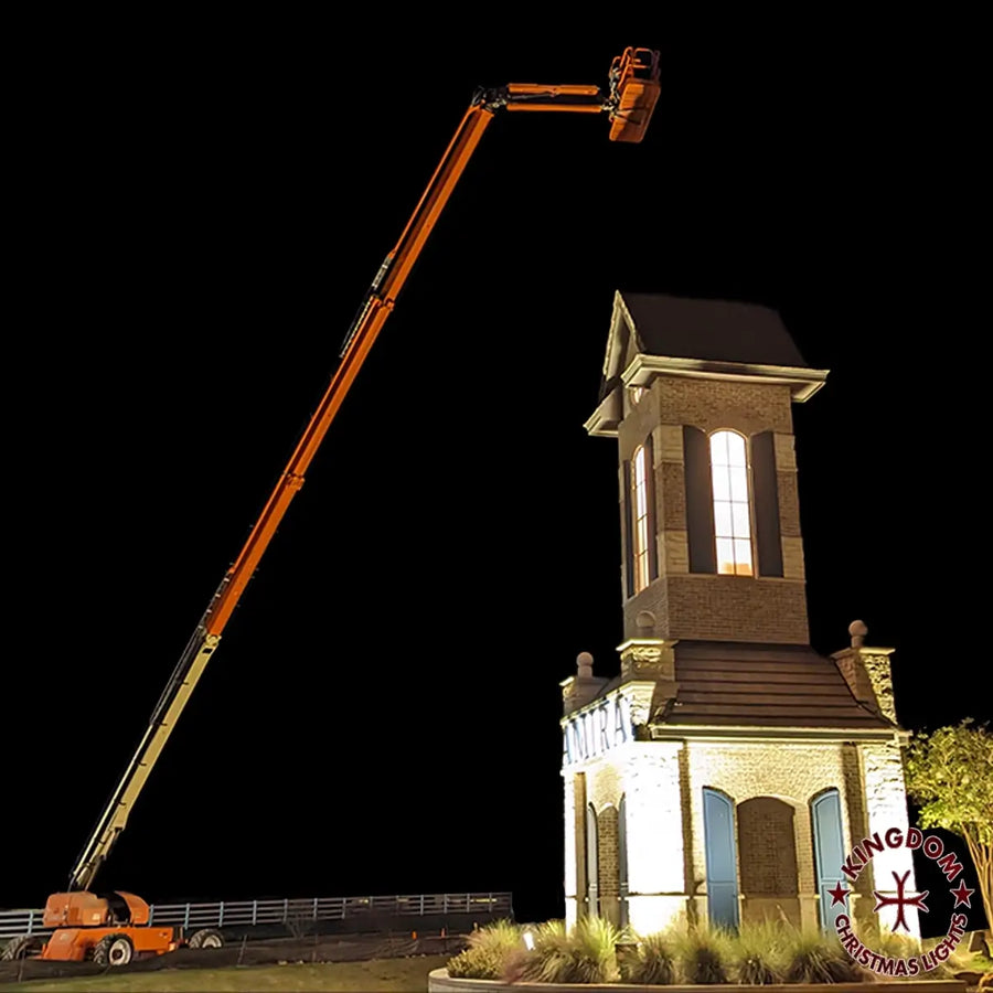A commercial boom lift being used to install Christmas lights on a tall structure at night.