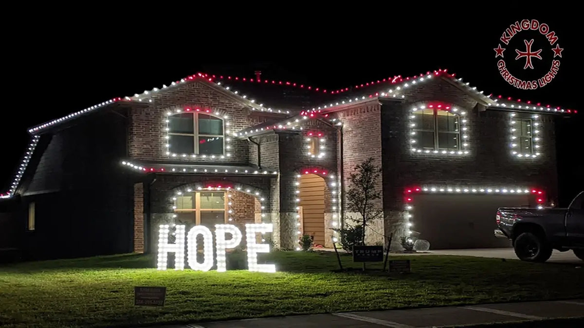 Two-story Houston-area home with red and white roofline and window lights, plus an illuminated HOPE display on the lawn.