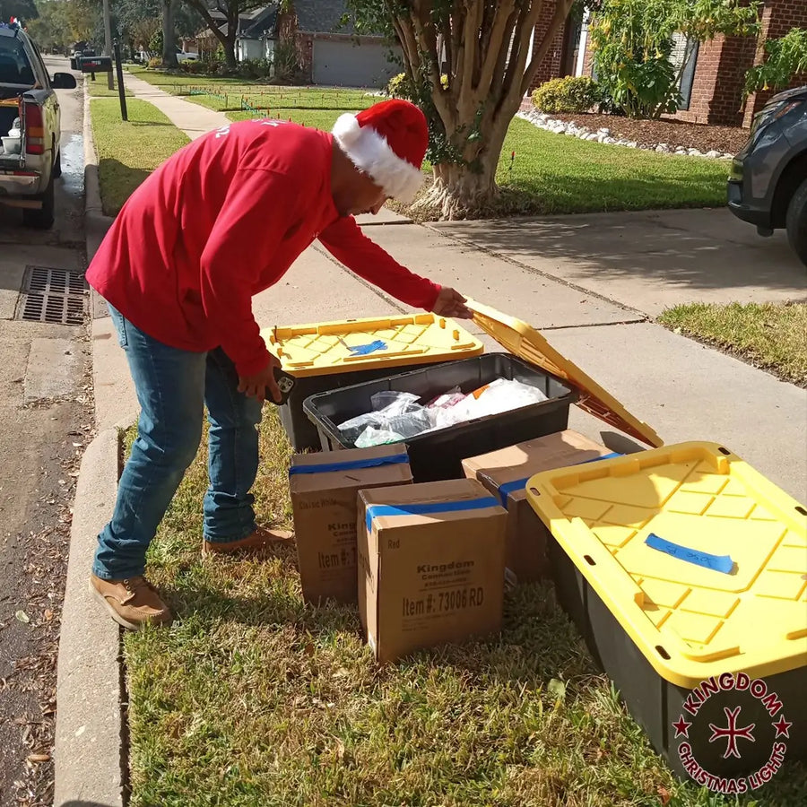 Person in red shirt and Santa hat sorting items from a yellow storage bin on a residential street.