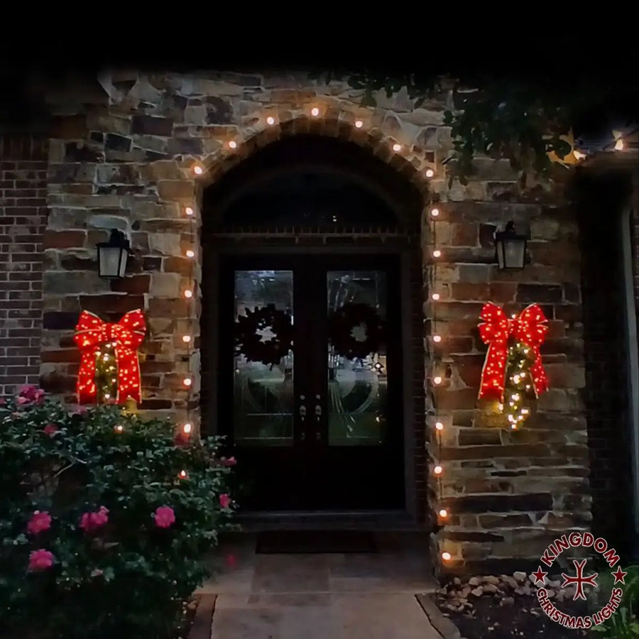 Decorative entrance with red bows and string lights on a stone wall.