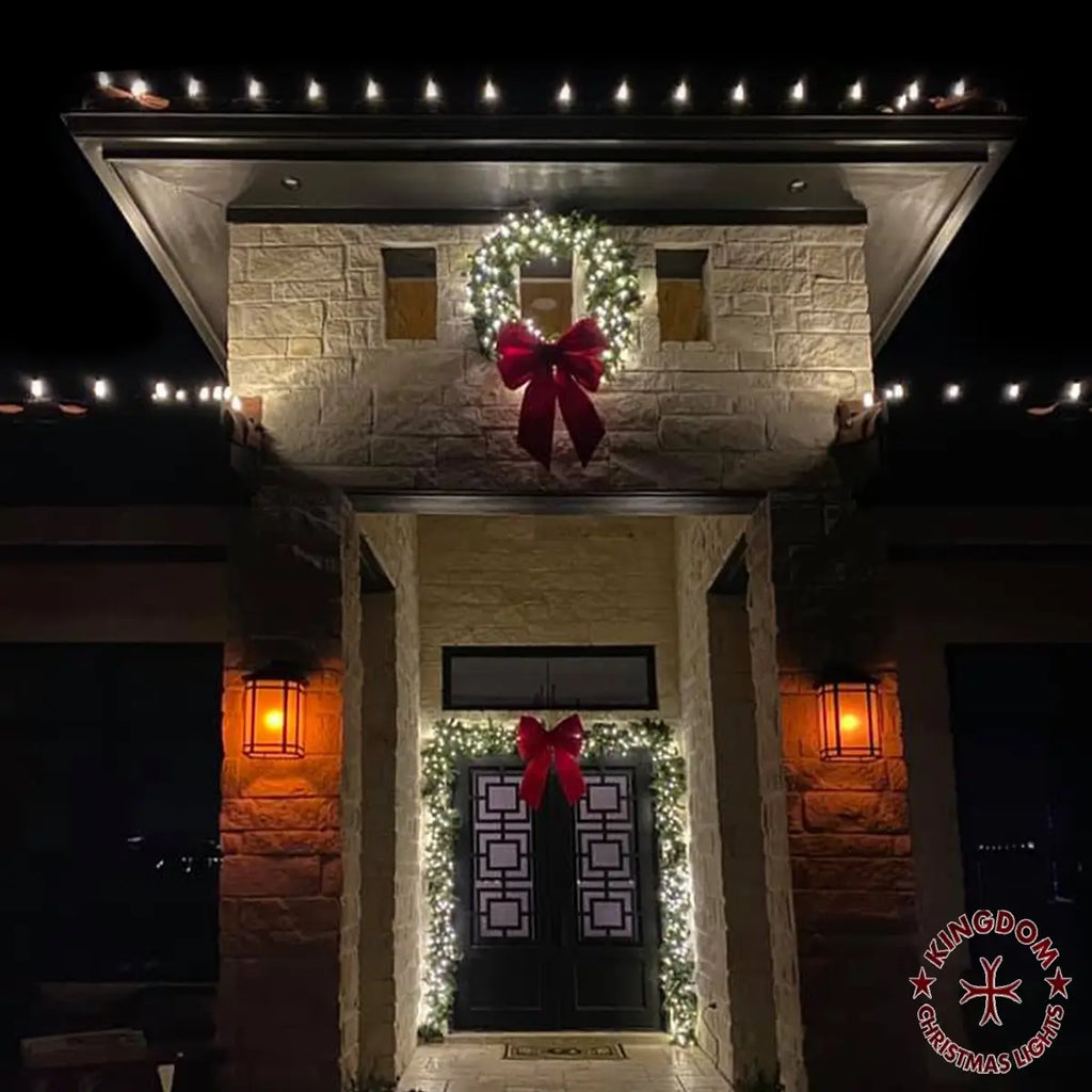 Decorative wreath with a large red bow on a stone building entrance at night.