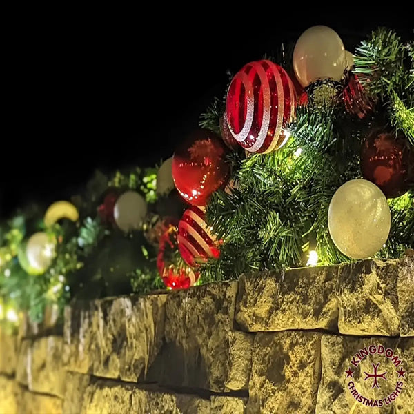 Decorative Christmas garland with ornaments on a stone ledge at night.