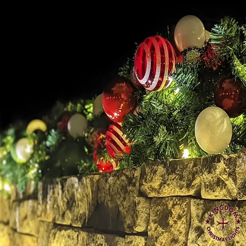 Decorative Christmas garland with ornaments on a stone ledge at night.
