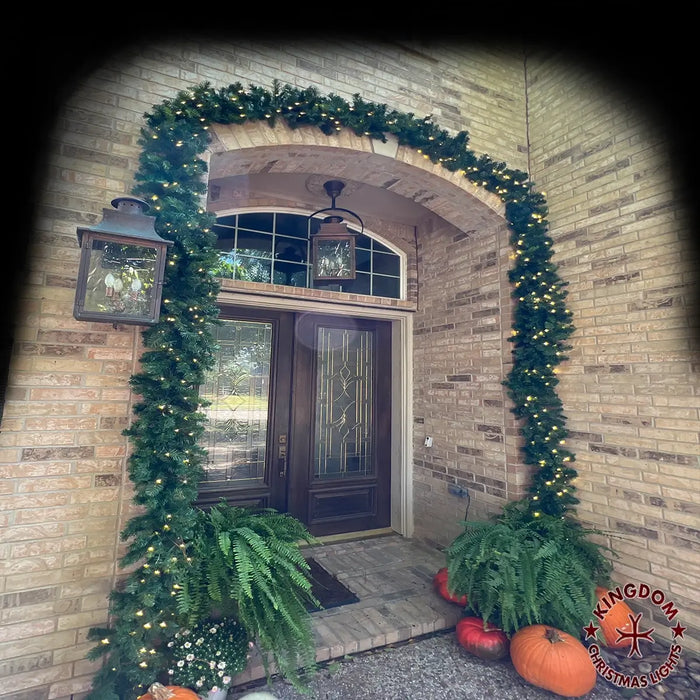 Decorative Christmas garland with lights and pumpkins on a brick wall.