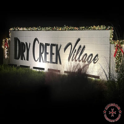 Sign for 'Dry Creek Village' with decorative lights and ribbons on a dark background