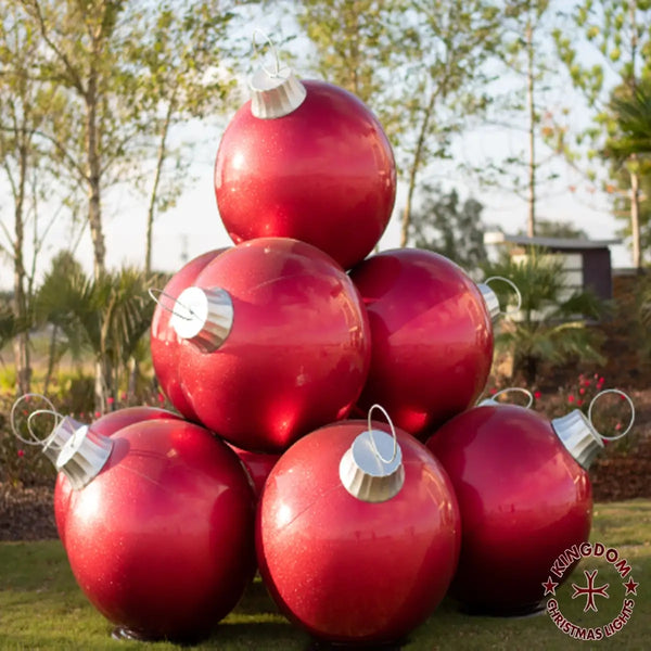 Stack of large red Christmas ornaments with silver caps on a grassy area.