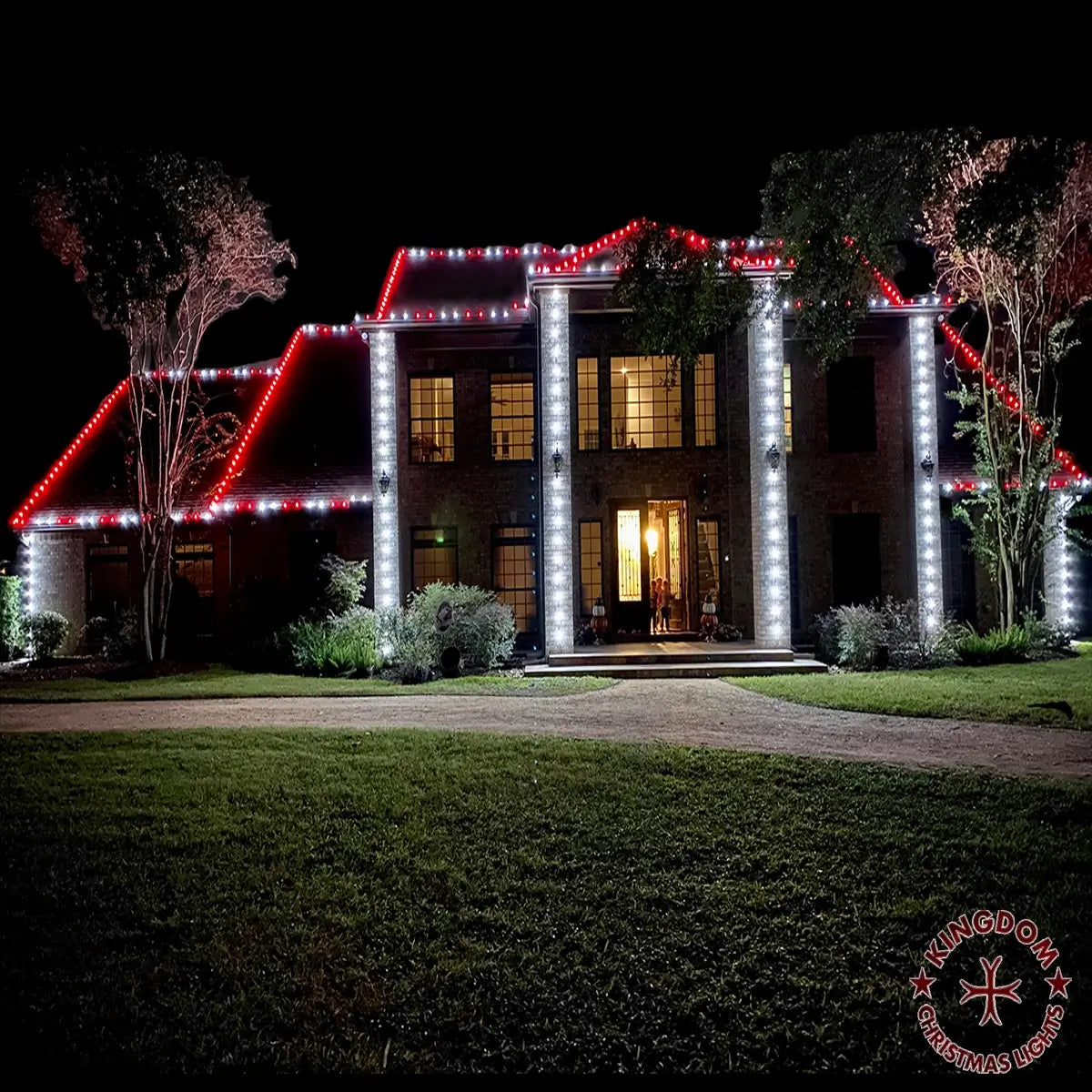 Two-story Katy home with red and white roofline lighting and white lights tracing tall front columns.