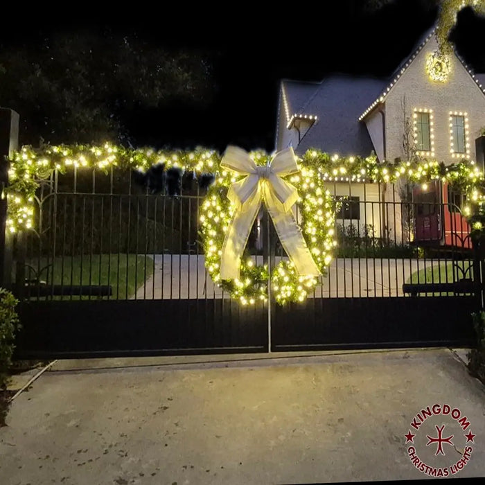 Decorative Christmas light setup with a large bow on a gate in front of a house.