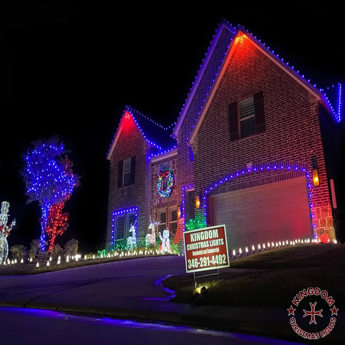 House decorated with colorful Christmas lights at night, with a Kingdom Christmas Lights sign in the foreground.