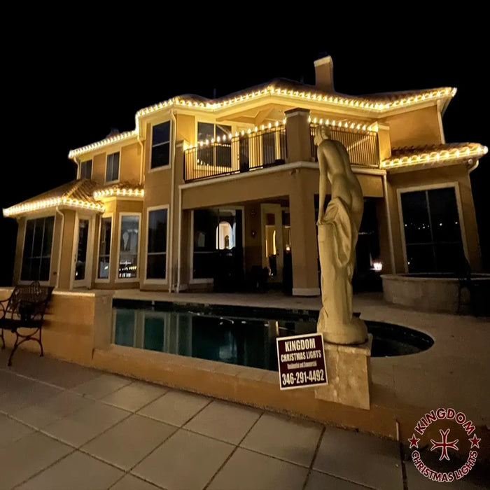 Luxurious house exterior with decorative lights, statue, and pool at night.