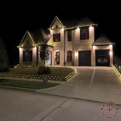 House exterior at night with Christmas lights and decorations, featuring a driveway and front yard.
