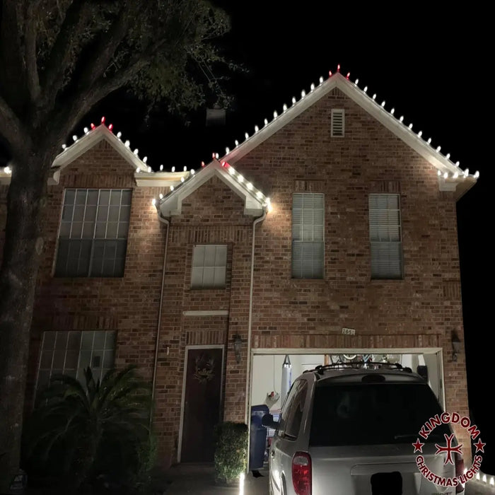 Brick house with Christmas lights on the roof at night, with a car parked in front.