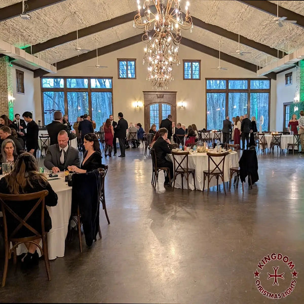 Large indoor event space with people dining and socializing, featuring a chandelier and large windows.